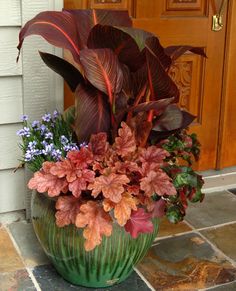 a green vase filled with lots of flowers sitting on top of a stone floor next to a door