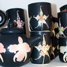 black teapots with flowers painted on them sitting on a shelf next to each other