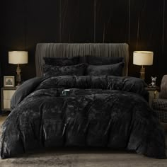 a bed with black comforter and pillows in a room next to two lamps on either side of the bed