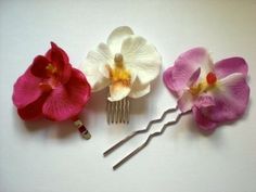 three flower hair pins are shown on a white surface