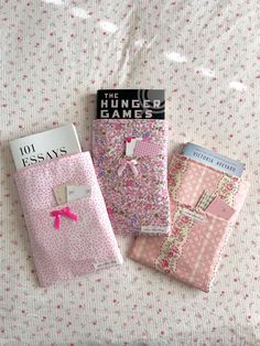 three books are laying on a bed with pink and white sheets, one has a pink bow