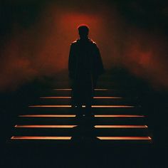 a man standing on steps in the dark with his back turned to the camera and light coming from behind him