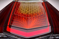 the rear end of a red car with an intricate design on it's hood