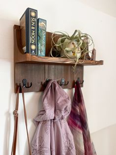 a coat rack with two coats hanging from it's sides and books on the top shelf