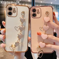 two women holding up their cell phones with heart charms attached to the back of them