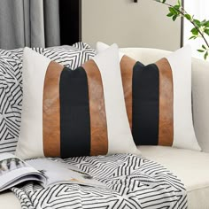 two black and white pillows sitting on top of a couch next to a plant in a vase