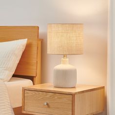 a white lamp sitting on top of a wooden table next to a night stand and bed