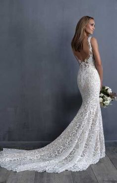 a woman in a white wedding dress standing against a gray wall with her back to the camera