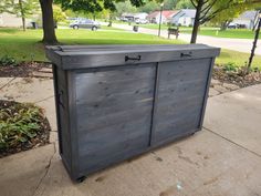 a wooden box sitting on top of a sidewalk next to a tree and grass field