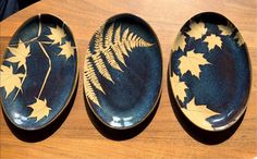 three plates with leaves painted on them sitting on a wooden table next to each other