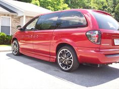 a red minivan parked in front of a house with black rims on it