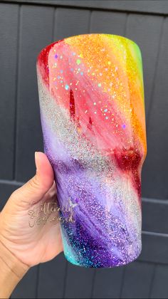 a hand holding up a rainbow colored cup with glitters on the outside and inside