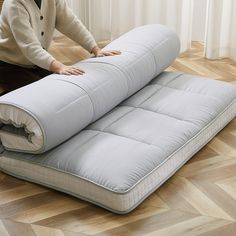 a woman sitting on the floor next to an inflatable mattress that is rolled up