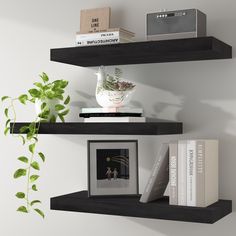 two black floating shelves with books, plants and other items on them in front of a white wall