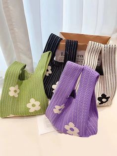 four bags in different colors and designs sitting on a table next to a white curtain