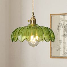 a green glass light fixture hanging from a wall next to a framed drawing on the wall