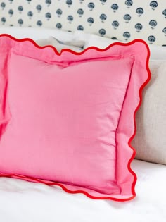 a bright pink pillow with scalloped edges on a white and blue patterned headboard