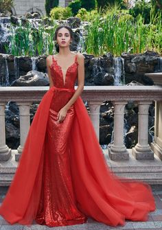 a woman standing in front of a fountain wearing a red dress with sequins