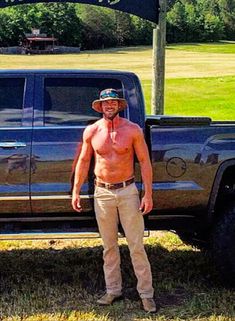 a shirtless man standing in front of a truck with no shirt and hat on