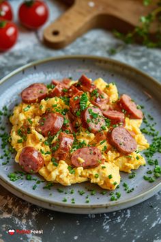 scrambled eggs with sausage and chives on a gray plate next to tomatoes, parsley