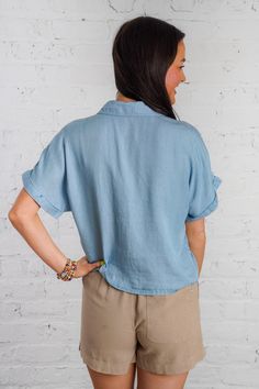 Ride the waves of style with our Drifting Tides Top. This blue chambray top features a button down front, a tie detail, and a front pocket, perfect for a casual yet chic look. The short cuffed drop sleeves and collared neckline add a touch of charm, while the soft chambray material provides ultimate comfort. Pair with our Sand Dune Shorts and Sunbeam Raffia Mules to complete the look! This top is lightweight, non-sheer, and has a loose boxy fit. 100% Tencel Brand- Be Cool Model is 5'5" and is we Washed Blue Chambray Button-up Top, Chic Light Wash Top With Pockets, Chic Light Wash Tops With Pockets, Spring Tops With Rolled Sleeves And Camp Collar, Spring Camp Collar Tops With Rolled Sleeves, Washed Blue Top With Button Closure For Day Out, Summer Denim Collared Blouse, Summer Collared Denim Blouse, Washed Blue Tops With Button Closure For Day Out