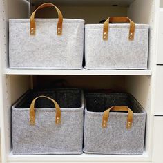 two canvas storage bins with leather handles in a white shelving unit filled with fabric baskets