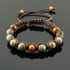 two bracelets with beads and brown cords on a black surface, one has an orange bea