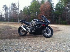 a black motorcycle parked on top of a gravel field next to trees and grass covered ground