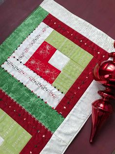 a red vase sitting next to a quilted table runner