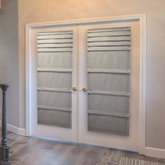 two white doors with blind shades on them in a living room next to a lamp