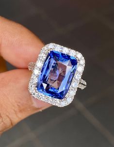 a woman's hand holding an engagement ring with a blue and white stone surrounded by diamonds