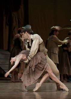 a man and woman dancing on stage with other people in the back ground behind them