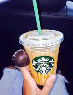 a person holding a starbucks drink in their hand with a chocolate covered cookie on the side