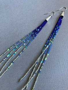 three strands of beads are hanging from silver earwires on a gray surface with blue and green beads