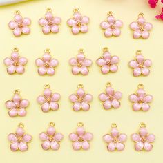 pink flower charms sitting on top of a yellow table next to flowers and a white plate