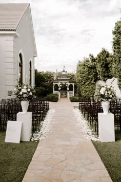 an outdoor ceremony setup with chairs and white flowers in vases on the aisle leading up to the chapel