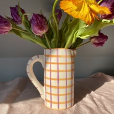 a vase with flowers in it sitting on a tablecloth covered bed sheet, next to a wall