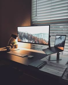 a desk with a laptop, monitor and keyboard on it in front of a window