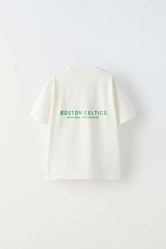 a white t - shirt with boston celtics on the front and green lettering on the back