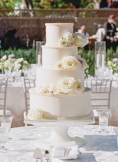 a wedding cake with white flowers on the top is surrounded by other tables and chairs