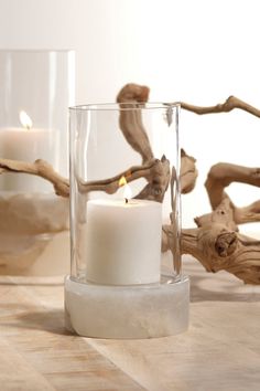 two white candles sitting in glass vases with driftwood behind them on a table