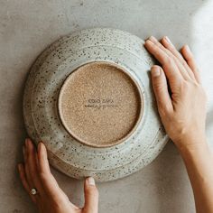 two hands are touching the bottom of a ceramic plate with writing on it and another hand is holding one