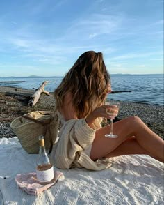 a woman sitting on top of a beach next to a bottle of wine