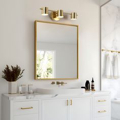 a bathroom with white and gold fixtures, marble counter tops and large mirror over the sink