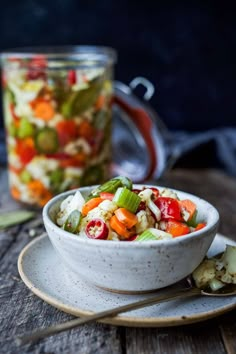 a white bowl filled with vegetables on top of a wooden table next to a glass jar