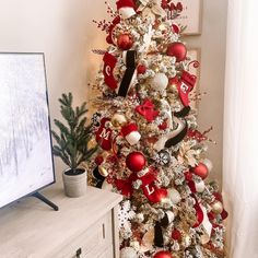 a white christmas tree with red and gold ornaments in front of a flat screen tv