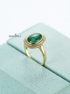 a gold ring with a green stone in the center on top of a blue box