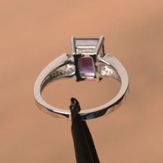 It is a natural amethyst ring. The main stone is 7 mm* 9 mm emerald cut.weight about 2.21 carats. The basic metal is sterling silver and plated with rhodium. To change the metal to a solid gold (white/rose) or platinum is also available, please ask for a quotation if you want. You can also go to my shop Home for more elegant rings: https://www.etsy.com/shop/godjewelry?ref=hdr_shop_menu Amethyst is February birthstone More amethyst rings: https://www.etsy.com/shop/godjewelry?ref=seller-platform-m Classic Emerald Cut Purple Rings, Classic Purple Emerald Cut Rings, Purple Baguette Cut Rings For Formal Occasions, Classic Purple Square Cut Ring, Amethyst Ring With Rectangular Purple Stone For Anniversary, Purple Amethyst Ring With Rectangular Stone For Anniversary, Rectangular Silver Amethyst Gemstone Ring, Emerald Cut Tanzanite Ring With Prong Setting, Formal Solitaire Amethyst Ring With Emerald Cut