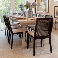 a dining room table with chairs and vases on it's centerpiece in front of a window