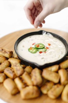 a person dipping sauce into a bowl of dip surrounded by bread sticks and cucumbers